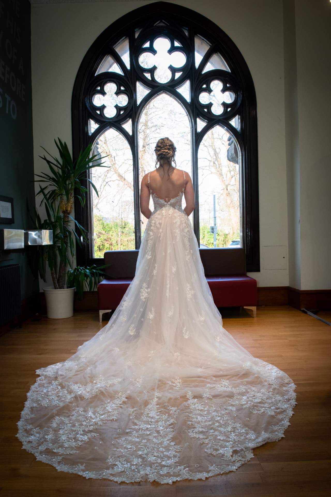 Bride in a lace gown with a long train in front of a gothic window at Eden Court